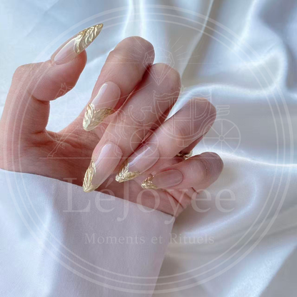 Side profile shot of the almond-shaped nails, showing the natural curvature and the subtle raised dimension of the textured gold art.