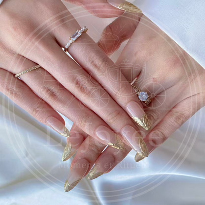 Elegant hand model wearing gold jewelry rings that complement the metallic gold french tip press-on nails, creating a sophisticated cohesive look.