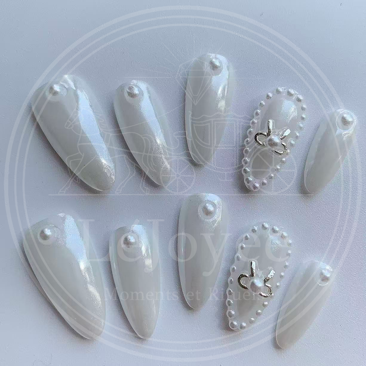 Close-up of the accent nail showing a minimalist silver bow center surrounded by a ring of tiny pearls on a shimmering satin-white base.