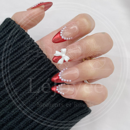 Luxury handmade press-on nails "Rouge Coquette" featuring metallic red french tips, delicate pearl lining, and large white 3D ribbon bows.