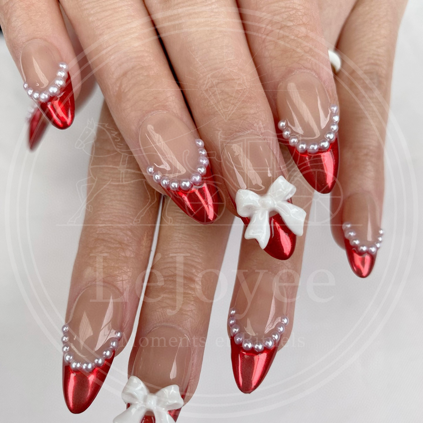 Close-up of the accent nail featuring a 3D white ribbon bow charm placed centrally on a metallic red french tip.