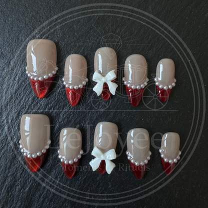 A full set of 10 almond-shaped press-on nails displayed on a dark stone background, highlighting the contrast between the shiny red tips and the matte white bows.