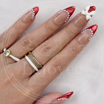 Stylish hand pose wearing gold and white rings that complement the pearl and red details of the Rouge Coquette luxury nail set.
