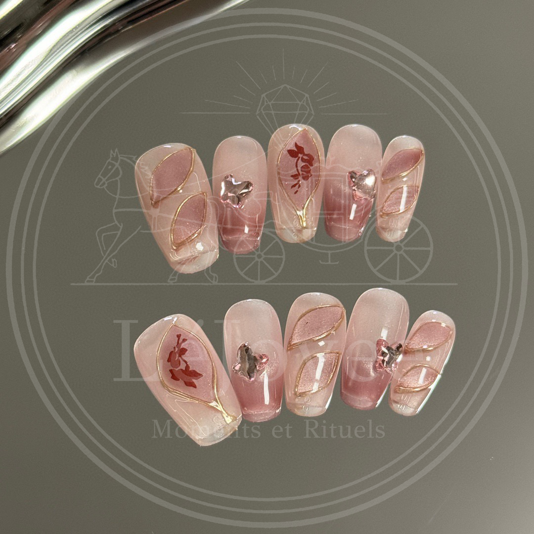 Shot of delicate pink rhinestone butterfly embellishments and gold-outlined abstract leaf patterns on glossy press-on nails.