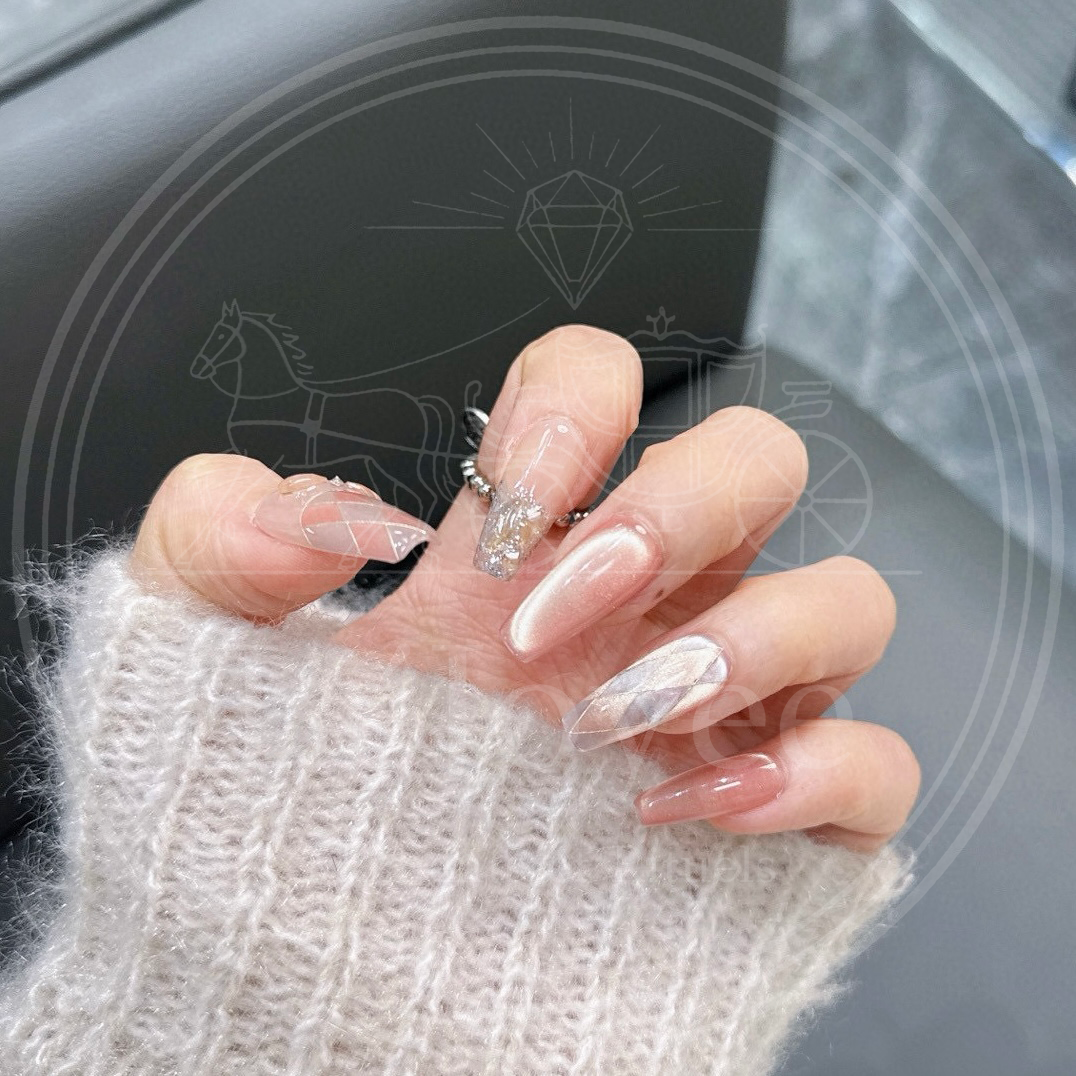 Top-down view of a hand wearing long coffin press-on nails. The design includes shimmering peach cat-eye, sheer argyle and champagne glitter accents.