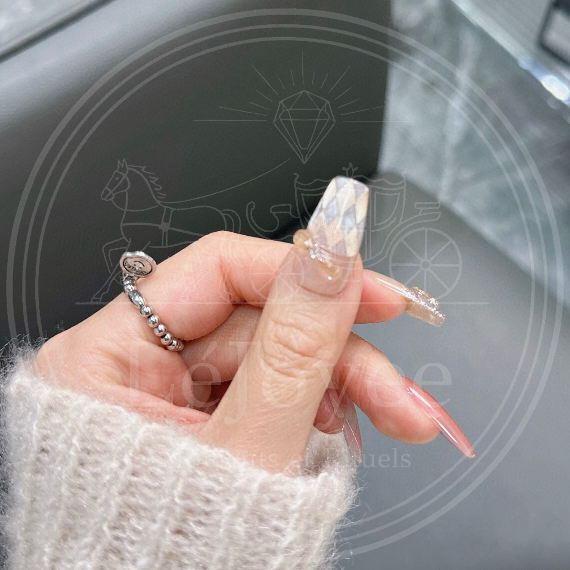 Detail shot focusing on the thumb nail, featuring a clear 3D bow charm with a rhinestone center placed over a sheer nude and white argyle pattern.