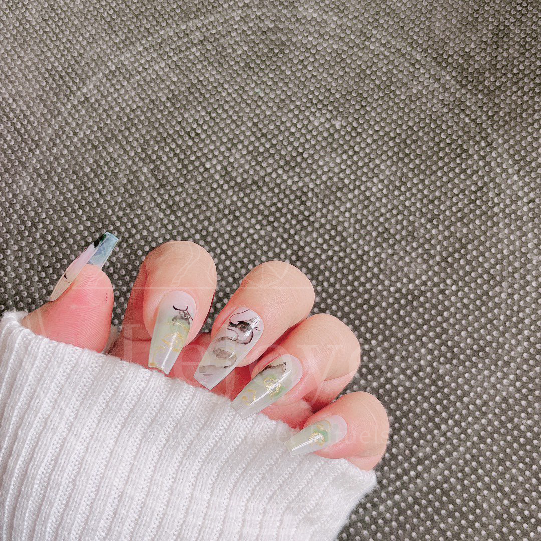 Artistic flatlay of the custom press-on nail set, highlighting the translucent sheer base and the fluidity of the black ink brushstrokes against the gold details.