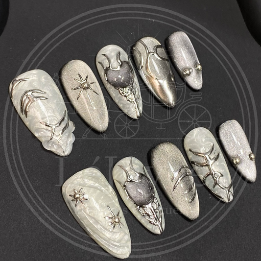 Handmade gothic-style press-on nails featuring silver magnetic cat-eye polish, 3D chrome tribal lines, and metallic heart accents on a marble grey base.