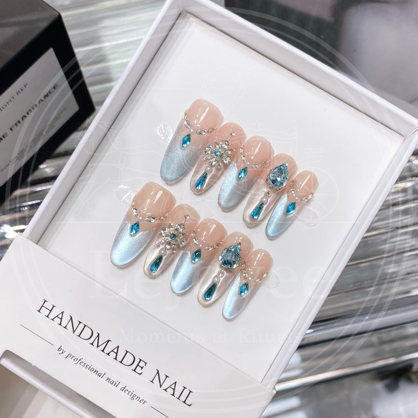 Luxury long almond press-on nails "Crystalline Azure" featuring an icy blue cat-eye ombre base, intricate snowflake rhinestone clusters, and large aquamarine teardrop gems with pearl accents.