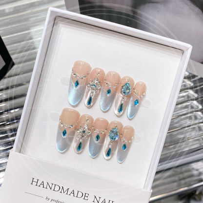 Close-up of the elaborate rhinestone arrangement showing a sparkling snowflake center and a hanging blue rhinestone pendant charm on frosted blue handmade nails.