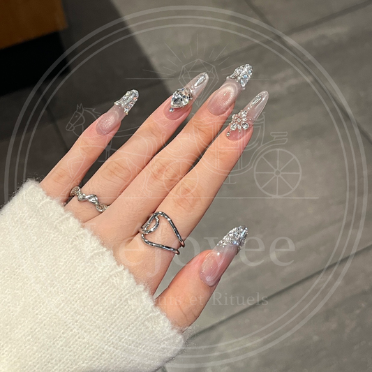 Luxury long stiletto press-on nails "Frozen Reverie" featuring a sheer blush base, silver magnetic cat-eye tips, and large 3D rhinestone heart charms