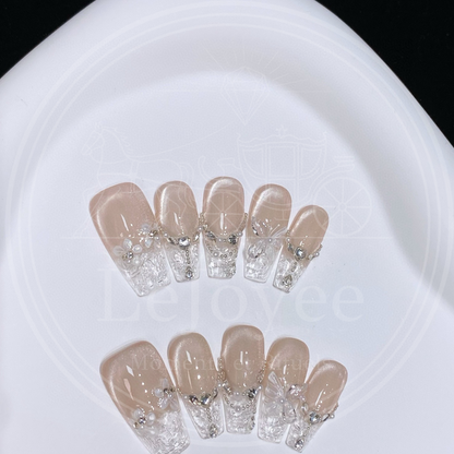 Luxury handmade press-on nails "Glass Serenade" featuring clear "shattered glass" textured french tips, champagne cat-eye base, and delicate pearl garland accents