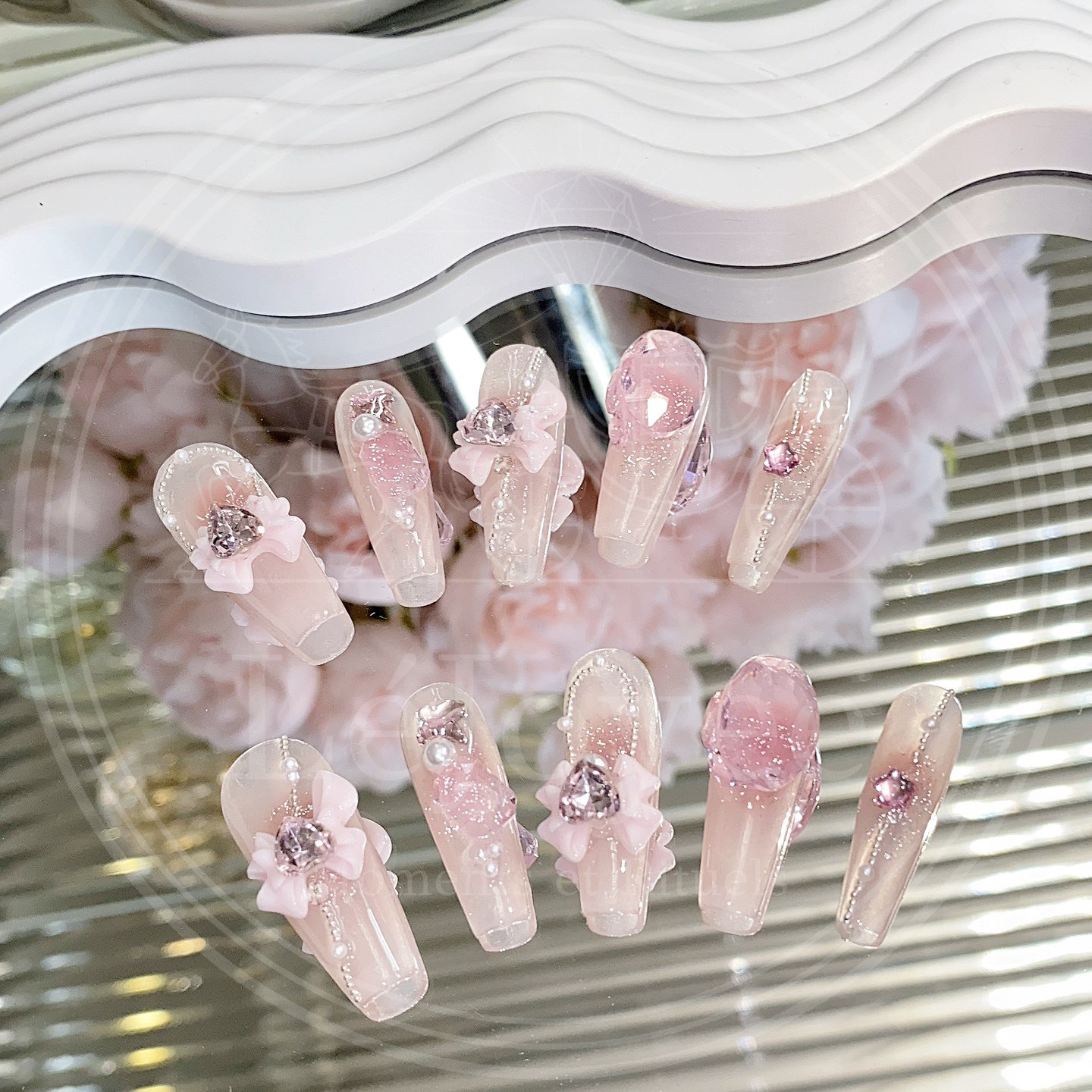 A detailed view of Rosy Reverie pink press-on nails featuring floral bows, rhinestones, and soft shimmer for a romantic, elegant look.