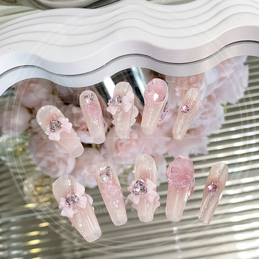 A detailed view of Rosy Reverie pink press-on nails featuring floral bows, rhinestones, and soft shimmer for a romantic, elegant look.