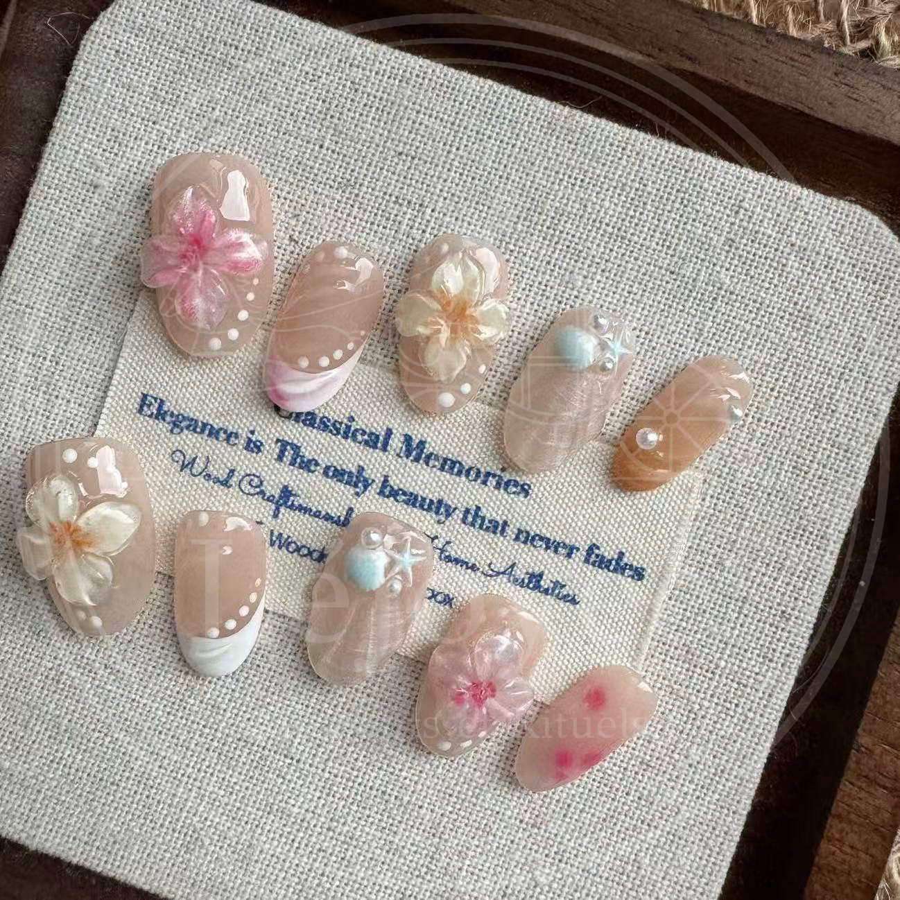 An artistic flatlay display of the full "Sakura Shores" nail set, showing the variety of varied designs including floral charms, seashell textures, and blush patterns.