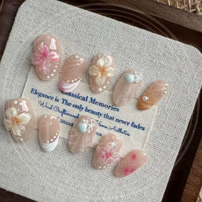 An artistic flatlay display of the full "Sakura Shores" nail set, showing the variety of varied designs including floral charms, seashell textures, and blush patterns.
