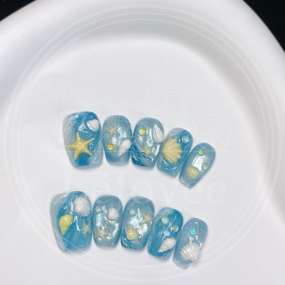 Close-up of 3D white shells and yellow starfish accents on a glossy blue water-ripple effect nail base.