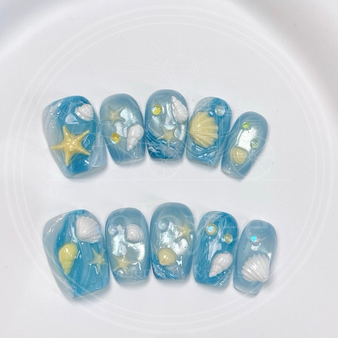 Luxury handmade press-on nails "Seafoam Daydream" featuring ocean blue marble art, 3D starfish, and seashell charms on short square nails.