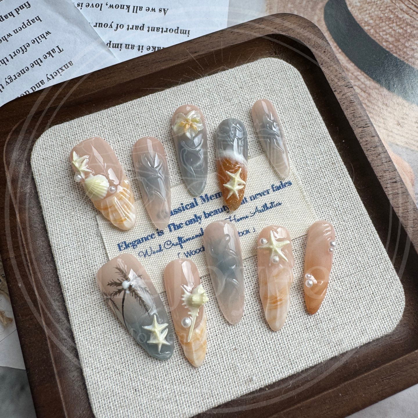 Luxury handmade press-on nails "Sunset Cove" featuring hand-painted palm tree silhouettes, 3D shell textures, and ocean-themed starfish charms