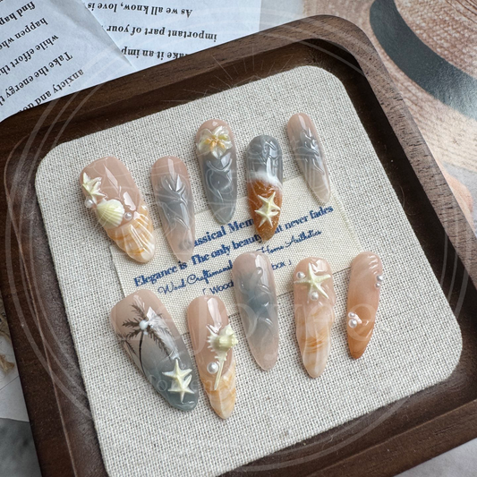 Luxury handmade press-on nails "Sunset Cove" featuring hand-painted palm tree silhouettes, 3D shell textures, and ocean-themed starfish charms