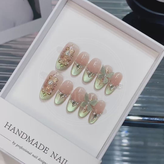 Close-up of ornate gold filigree frames and V-shaped rhinestones french tips on shimmering green and nude gradient nails, capturing a vintage royal aesthetic