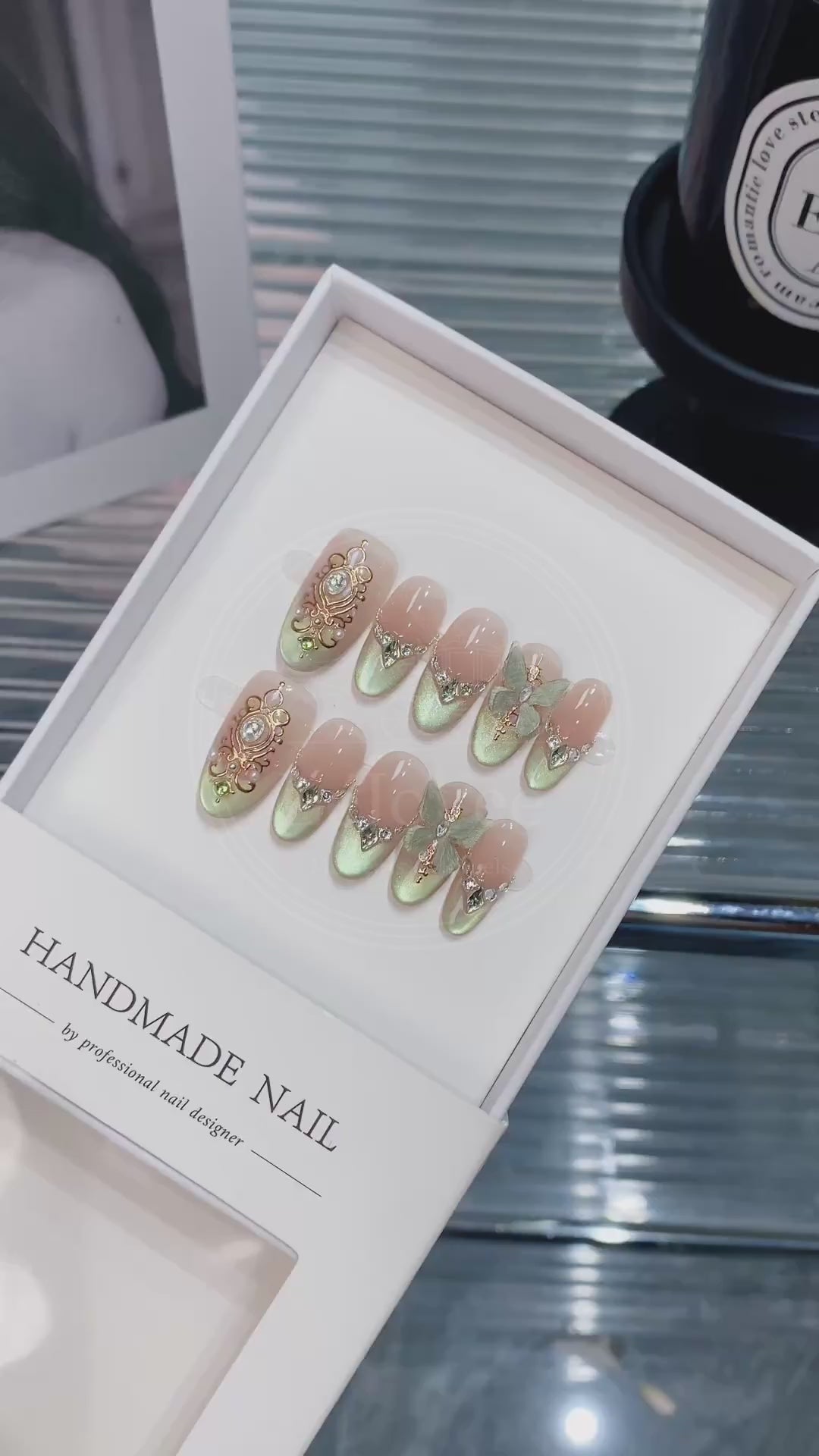 Close-up of ornate gold filigree frames and V-shaped rhinestones french tips on shimmering green and nude gradient nails, capturing a vintage royal aesthetic