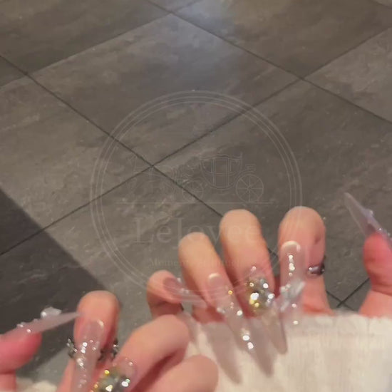 A detailed view of Lustre Bloom nude press-on nails showcasing rhinestone sparkle, layered chain details, and soft gradient.