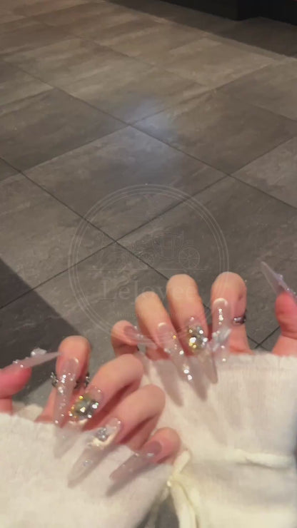 A detailed view of Lustre Bloom nude press-on nails showcasing rhinestone sparkle, layered chain details, and soft gradient.